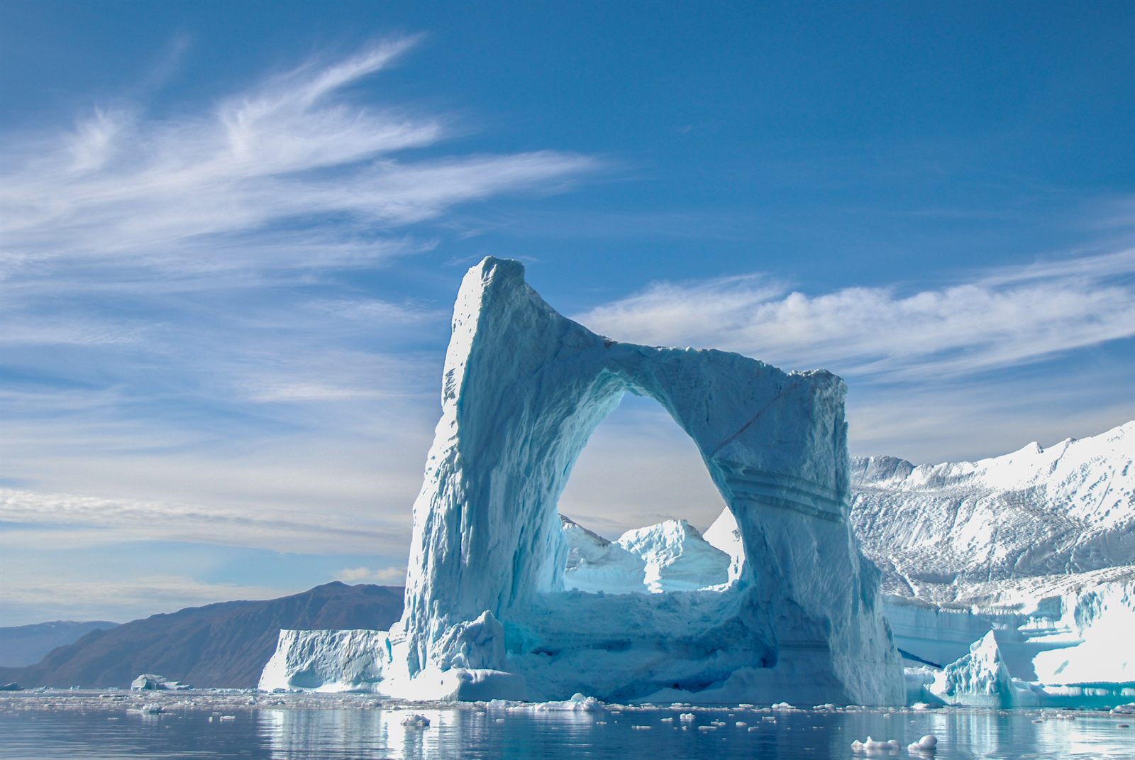 Huge iceberg with a natural arch floating in front of snowy Arctic mountains