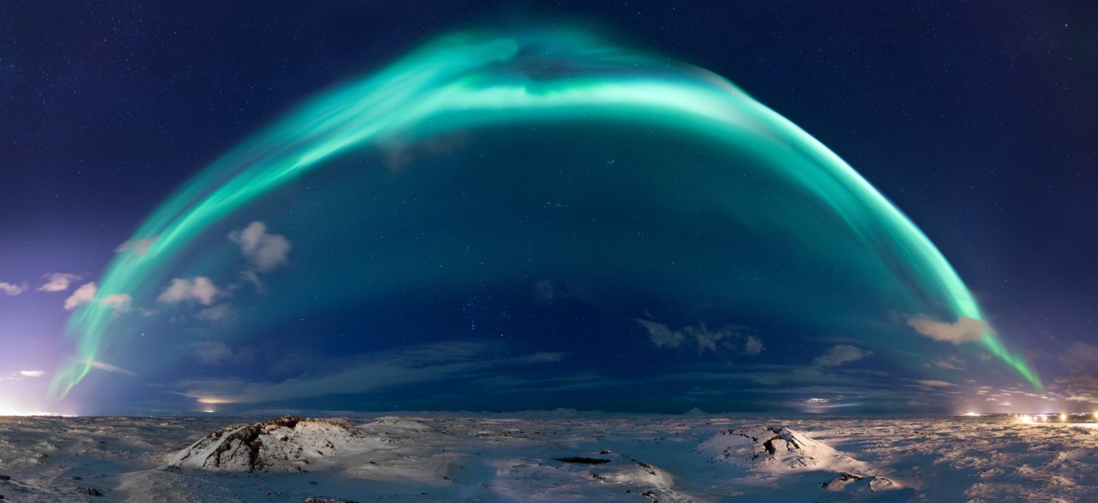 Arc of green northern lights over an icy shoreline at night