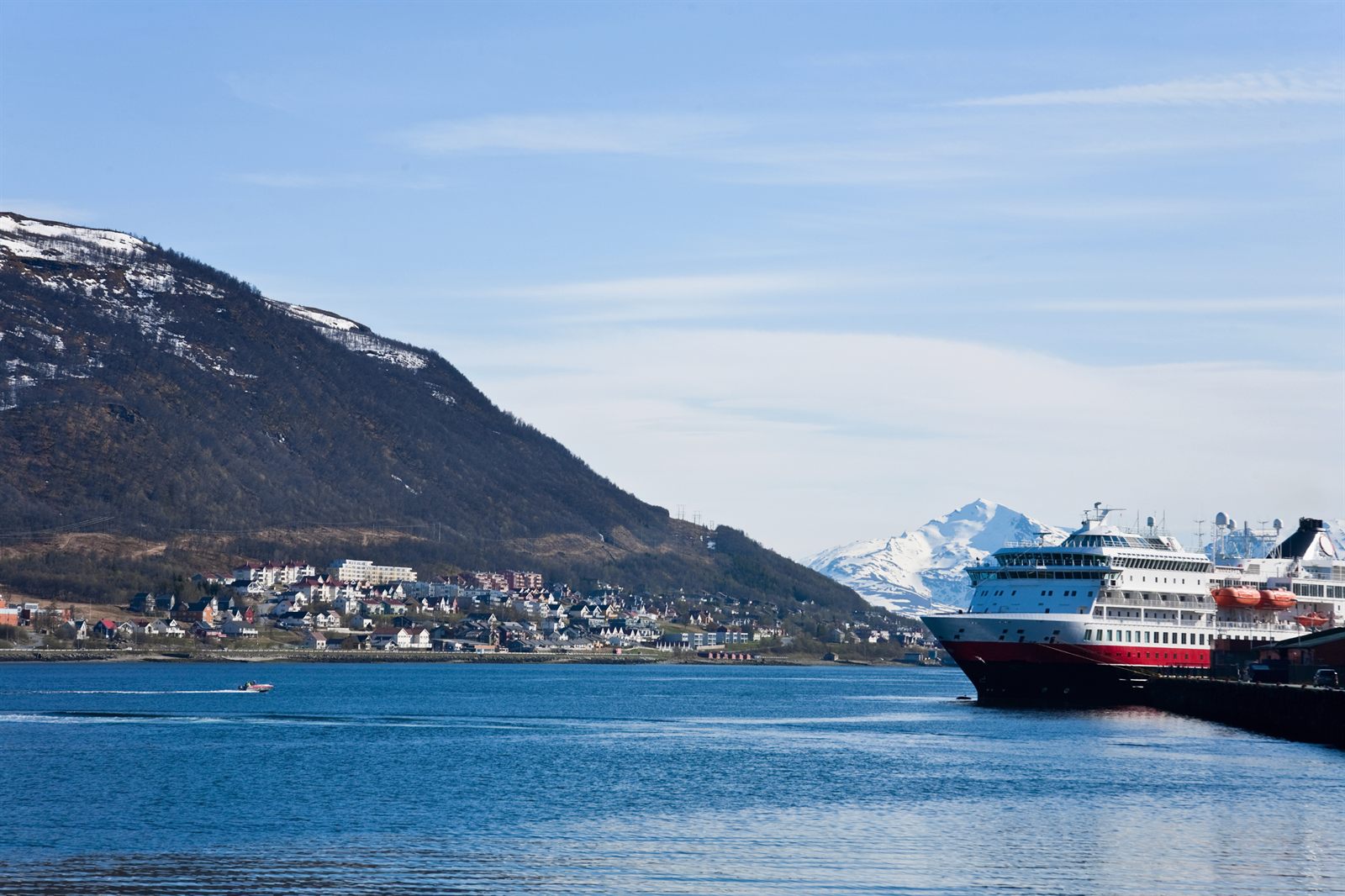 Norwegian coastal ship berthed below snow-streaked mountains in Tromso