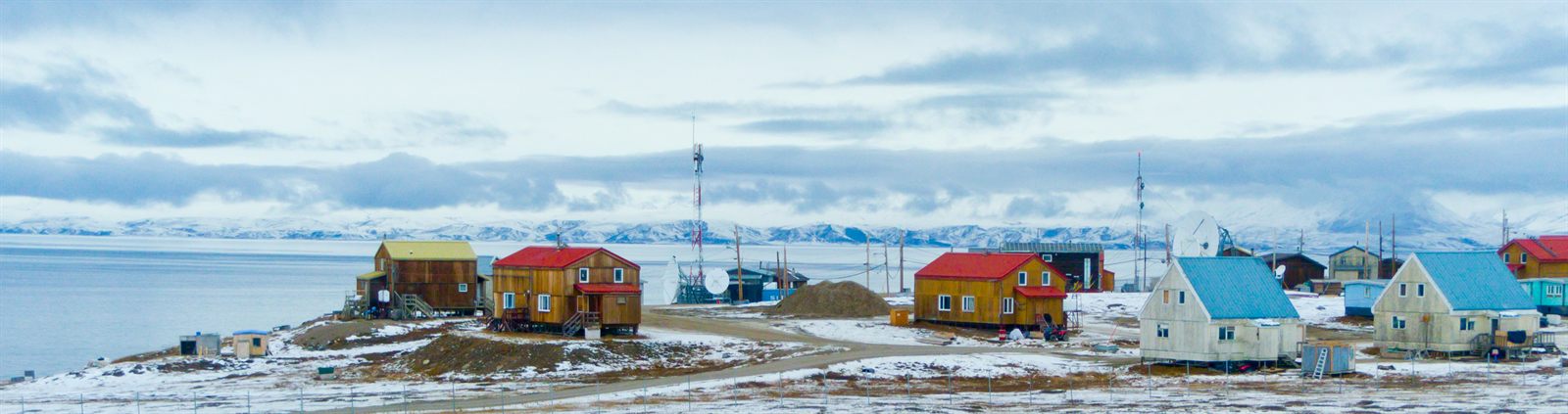 Brightly painted wooden houses and radio masts of a remote Arctic settlement beside a frozen fjord